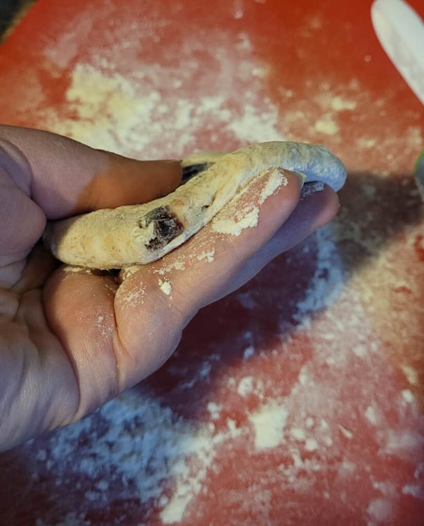 A rolled out piece of dough held to show the thickness. It is a little less than half an inch thick.