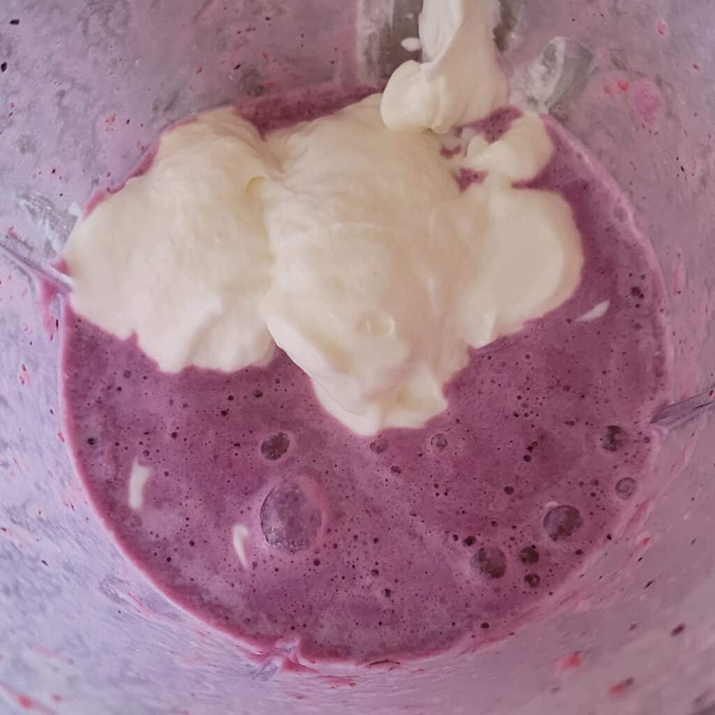 Purple liquid in the bottom of a blender, from blending frozen strawberries, blueberries and bananas with milk. Yogurt has been added but not yet blended.