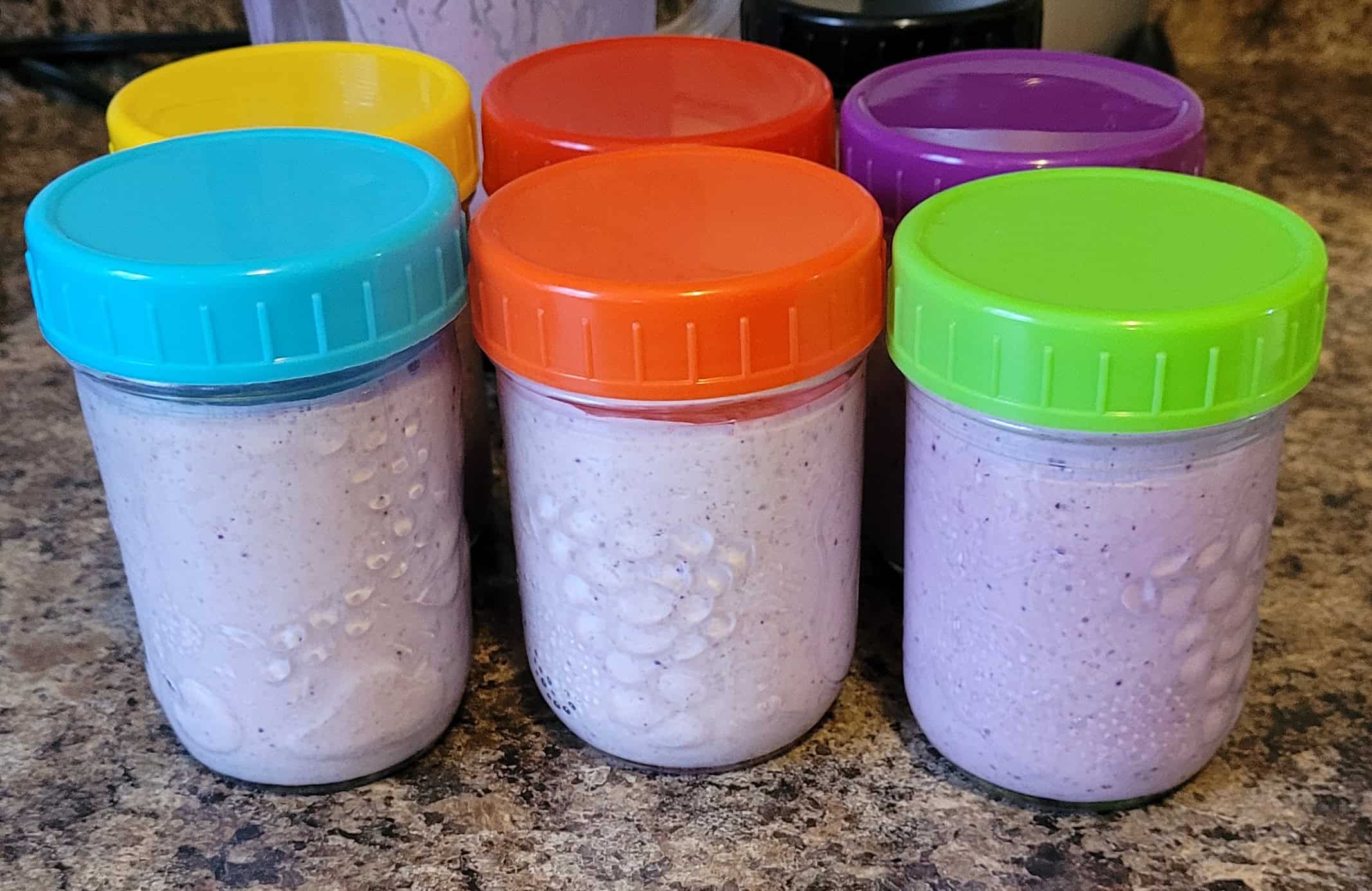 Half pint mason jars with colourful plastic lids, filled with light purple-ish yogurt drinks.